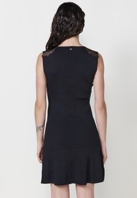 Schwarzes ärmelloses Kleid mit geripptem Textil, das mit Spitzenakzenten an den Schultern und einem ausgestellten Saum versehen ist.