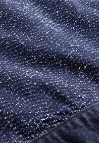 Tamsiai mėlyna medžiaga su baltais taškeliais, rodanti tekstūruotą paviršių ir siuvimo siūlės detales.