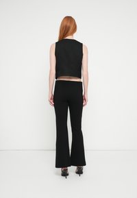 Mustast lühendatud varrukateta top mustade volditud pükstega. Kangas näib olevat sile, puhta disainiga, ning pükstel on kohandatud vöökoht.