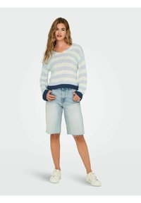 Gestreepte gebreide trui in lichtblauw en wit, met een V-hals en een donkerblauwe zoom. Gecombineerd met lichtdenim bermuda shorts en witte sneakers.