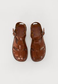Brune lærsandaler med åben design, der har vævede stropper, justerbar sidebuckle og flade såler. Glat tekstur med en naturlig finish.
