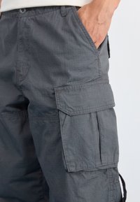 Grå cargobyxor i texturerad tyg, med sidofickor, avslappnad passform och en subtil rutmönster på ytan.