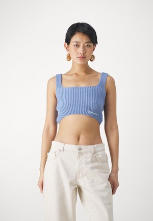 Haut en tricot bleu clair raccourci avec décolleté carré et côtes texturées, associé à un jean à taille haute et pattes d'éléphant écru.