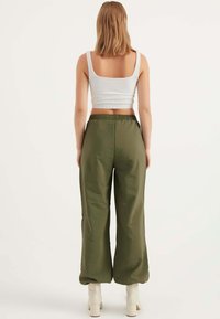 Olijfgroene, wijde broek met een elastische taille. Gecombineerd met een aansluitend, wit geribbeld tanktop. Soepele textuur en casual ontwerp. Witte hakken.