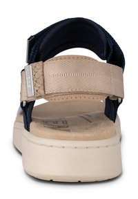 Beige och marinblå sandal med en texturerad vävd rem, justerbar bakrem och en mjuk korkfotbädd. Förhöjd gummisula och logotypdetalj.