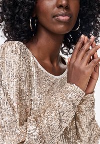 Złoty top z cekinami, z okrągłym dekoltem i bufiastymi rękawami, charakteryzujący się gładką fakturą i dużymi cekinami, które zapewniają błyszczący efekt.