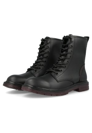 Paire de bottes de combat en cuir noir à lacets, semelles marron, bouts arrondis et tige montant à la cheville sur fond blanc.