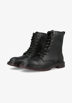 Paire de bottes de combat en cuir noir à lacets, semelles marron, bouts arrondis et tige montant à la cheville sur fond blanc.