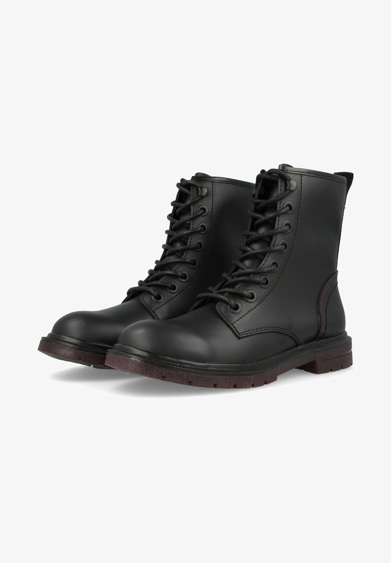 Paire de bottes de combat en cuir noir à lacets, semelles marron, bouts arrondis et tige montant à la cheville sur fond blanc.