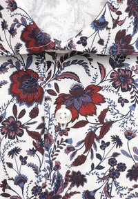 Col de chemise blanc avec un motif floral rouge et bleu et un bouton blanc fixé au centre.