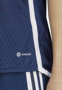 Maglietta sportiva della marina con motivo testurizzato, accenti bianchi sui lati e logo AEROREADY. Il tessuto sembra traspirante e ad asciugatura rapida.