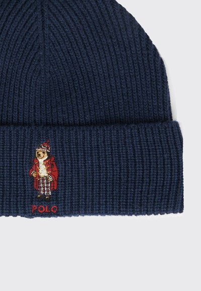 Beanie a maglia blu navy con texture a coste, che presenta un orso ricamato in un cappotto rosso e il testo "POLO" in rosso sotto il design.