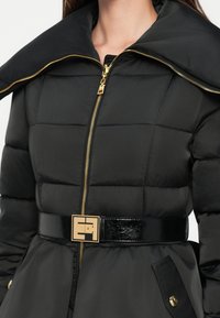 Black puffer coat with a wide collar, gold zipper, and glossy black belt featuring a gold logo. Textured fabric with quilted sections.