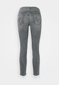 Vaqueros de mezclilla gris de corte ajustado con dobladillos deshilachados, que cuentan con dos bolsillos traseros con un diseño de cheurón. La tela tiene una textura de mezclilla clásica.