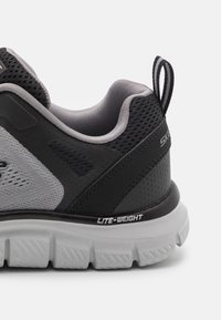 Black and gray sneaker with a mesh upper, textured panels, cushioned sole, and “LITE-WEIGHT” detailing. Features a pull tab on the heel.