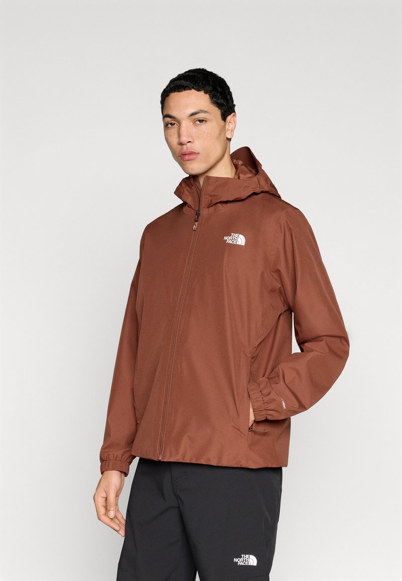 Καφέ αδιάβροχο μπουφάν με φερμουάρ μπροστά, ρυθμιζόμενη κουκούλα και ελαστικά μανίκια. Διαθέτει μικρό λευκό λογότυπο στο αριστερό στήθος.