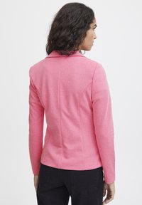 Blazer elasticizzato rosa con maniche lunghe, colletto a punta e vestibilità su misura. Presenta un tessuto testurizzato e dettagli delle cuciture lungo la schiena.