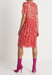 Červené květinové šaty s krátkými rukávy a vrstvenou sukní. V kombinaci s růžovými vysokými botami na podpatku. Průhledný zadní díl se květinovými detaily.