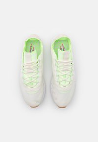 Chaussures de sport blanches avec des accents verts, tige en mesh, semelle texturée et détails réfléchissants. Les lacets sont intégrés dans le design.