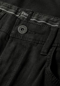 Pantalon noir à texture lisse, doté d'une fermeture à boutons et d'une étiquette indiquant "Flex On the go". Comprend un détail de ceinture rayée.