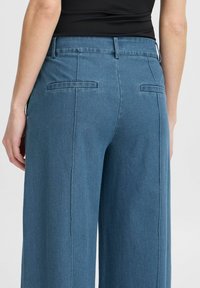 Lichtblauwe wijde denimtrousers met een schone tailleband, achterzakken en een zachte textuur met subtiele stikdetails.