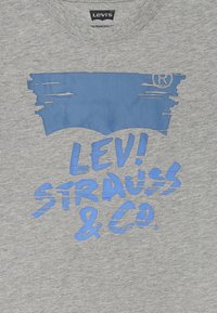T-shirt grigia in cotone con un design grafico blu che presenta il testo "LEVI! STRAUSS & CO." e un logo stilizzato in alto.