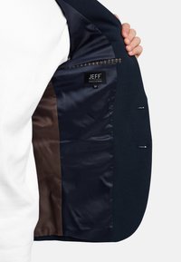 Giacca sportiva blu navy con fodera interna liscia marrone. Presenta un'etichetta con la scritta "JEFF", taglia 50, e due tasche interne. Vestibilità su misura.