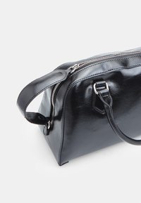 Borsa a mano in pelle nera con finitura lucida, chiusura con zip e doppi manici. Presenta una forma elegante e arrotondata con accenti hardware minimali.