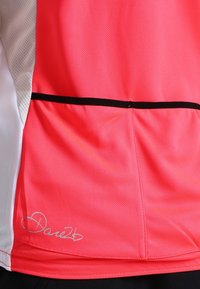 Różowa sportowa koszulka z poliestru z siateczkowymi panelami po bokach, czarnym obszyciem oraz srebrnym podpisem w prawym dolnym rogu.