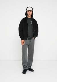 Sort fleece zip-up hoodie med store frontlommer, parret med en mørk grafisk t-shirt, grå løstsiddende jeans og sorte sneakers.