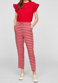 Top rosso texturizzato con maniche arricciate, abbinato a pantaloni rossi con motivo a zigzag bianco. Il modello indossa sneakers di colore chiaro.