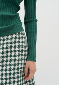 Zöld csíkos, hosszú ujjú felső zöld és fehér houndstooth mintás szoknyával párosítva. Közeli felvétel a kéz és az ujj részleteiről.
