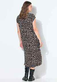 Pitkä leopardikuvioinen mekko beige ja musta, jossa on lyhyet hihat ja sivuhalkiot, yhdistettynä mustiin paksupohjaisiin saappaisiin.
