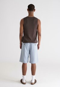Brown ribbed tank top, light blue shorts with button details, white socks, and brown sandals, viewed from the back against a plain background.