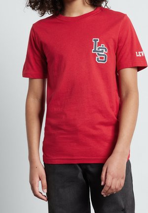 Camiseta roja de algodón con mangas cortas, que presenta un logo texturizado en blanco y negro en el pecho izquierdo y la palabra "LEVI'S" en la manga.