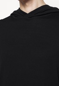 Felpa nera con una texture morbida e leggera, caratterizzata da un design a V e un cappuccio drappeggiato. Il tessuto appare liscio e versatile.