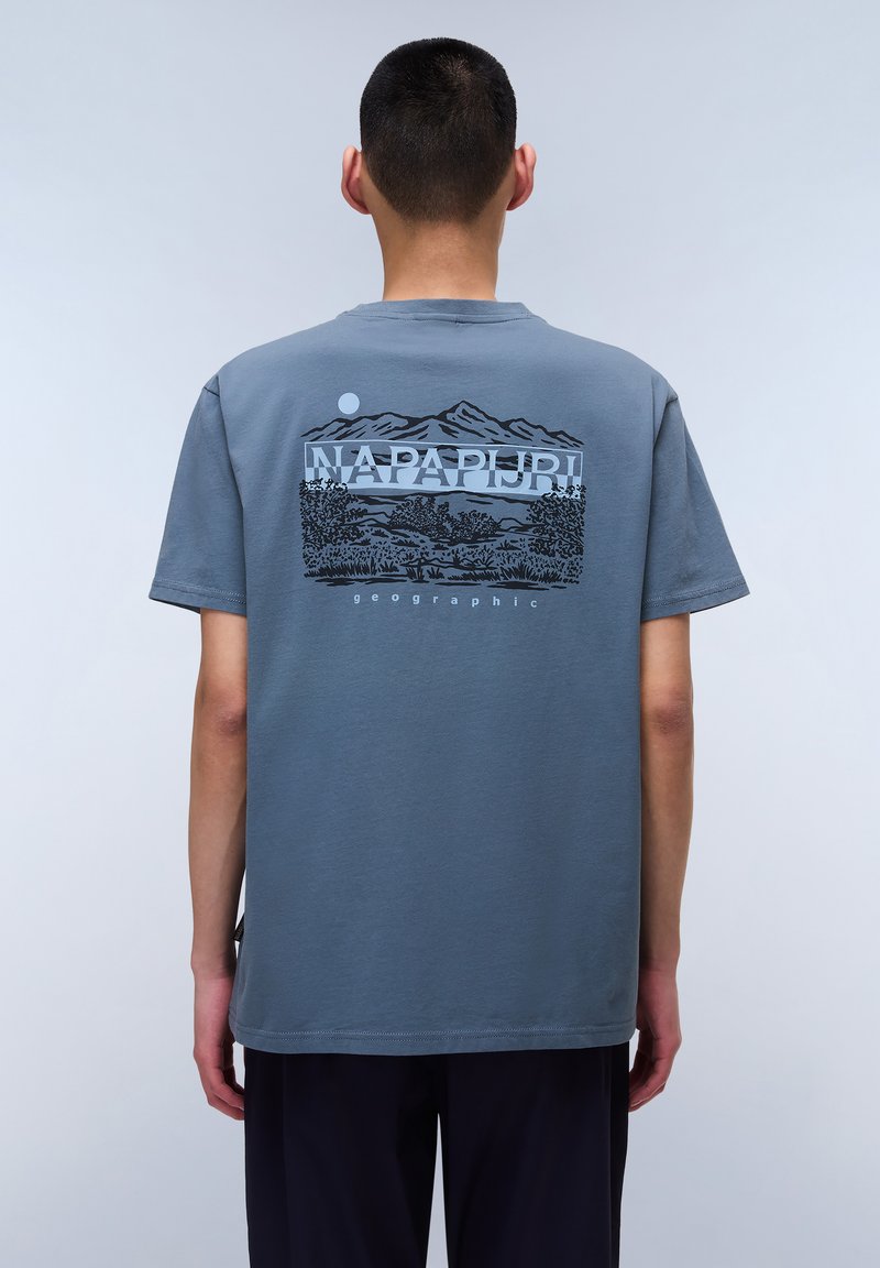 Camiseta de algodón gris con un diseño gráfico negro en la parte trasera, que representa montañas, árboles y el texto "NAPAPIJRI geographic."