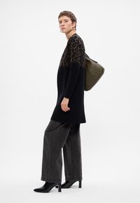 Dzianinowy sweter w czerni z górną częścią w leopardzi wzór, w połączeniu z szerokimi szarymi dżinsami i czarnymi botkami na obcasie. Olivowa torba.