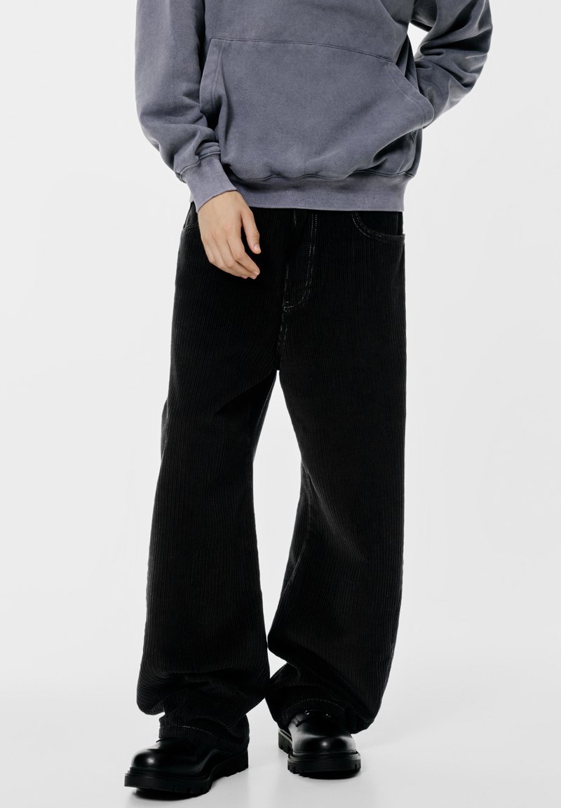 Pantaloni largi din corduroy negru cu nervuri verticale proeminente. Stilizați cu un hanorac gri; asortați cu cizme negre masive.