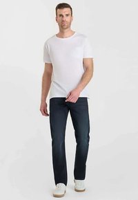 T-shirt blanc à manches courtes avec une poche poitrine, associé à un jean en denim foncé et des baskets blanches. Look décontracté dans l'ensemble avec une coupe ajustée.