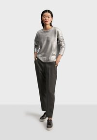 Silver, metallisk långärmad topp i kombination med mörkgrå skräddarsydda byxor med guldknappdetaljer, avslutat med svarta sneakers.