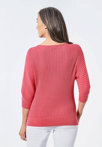 Rosaroter gerippter Pullover mit Dreiviertelärmeln. Merkmale sind strukturierte Linien und ein weiter Halsausschnitt. Weicher Strickstoff mit enger Passform.