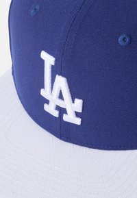 Gorra de béisbol azul con visera blanca que presenta el logotipo bordado "LA" en blanco. El material parece ser tejido con un acabado texturizado.