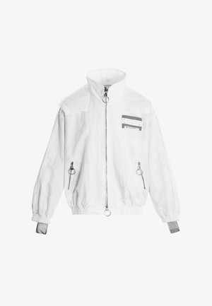 Chaqueta blanca con cremallera y cuello alto, dos bolsillos delanteros con cremallera y tiradores redondos, puños elásticos y una pequeña parche rectangular en el pecho.