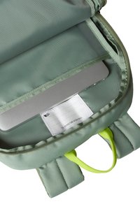 Light green backpack with a smooth exterior, padded straps, and a zipper closure. Contains a silver laptop and a label inside.