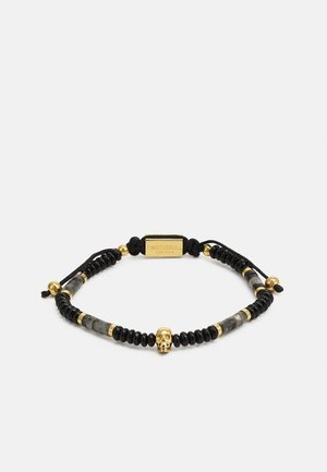 Verstellbares schwarzes Perlenarmband mit goldenen Akzenten und einem zentralen goldenen Totenkopf-Anhänger vor weißem Hintergrund.
