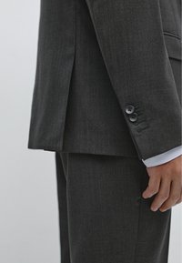 Completo grigio antracite con tessuto strutturato, design sartoriale, spacco laterale visibile e polsino con due bottoni neri.