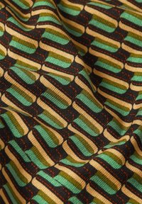 Textil mit geometrischem Muster in Grün, Schwarz und Beige. Die Textur erscheint gewebt, mit sichtbaren roten Nähakzenten.