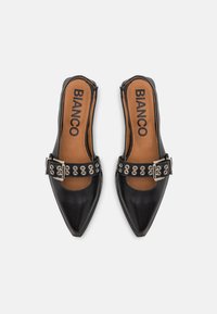 Svarta slingback-skor med spetsig tå, överdel i läder, beige innersula, spänne med silvernitar, slät textur. Varumärkesetikett synlig inuti.