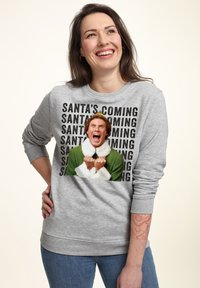 Šedá mikina s dlouhými rukávy, která má velký kreslený motiv postavy v zelené a bílé barvě, s opakujícím se textovým designem pod ní.